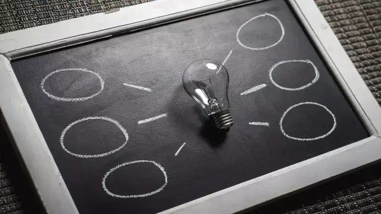 Die-hard fans article link and header image - Top-down view of lightbulb sitting on top of a small, rectangular chalkboard with idea bubbles drawn on it.